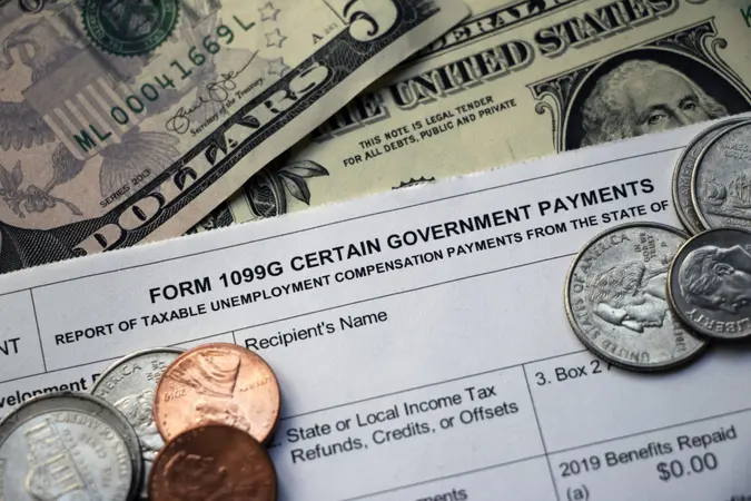 Closeup of the top of a tax Form 1099G Certain Government Payments - Taxable Unemployment Compensation Payments on top of cash with some coins scattered on top.