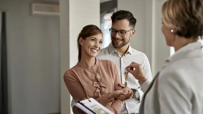 Happy couple buying new home and receiving house keys form real estate agent.