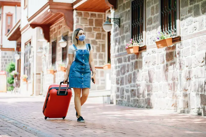 tourist Young woman wearing medical mask and walking with suitcase on the street.