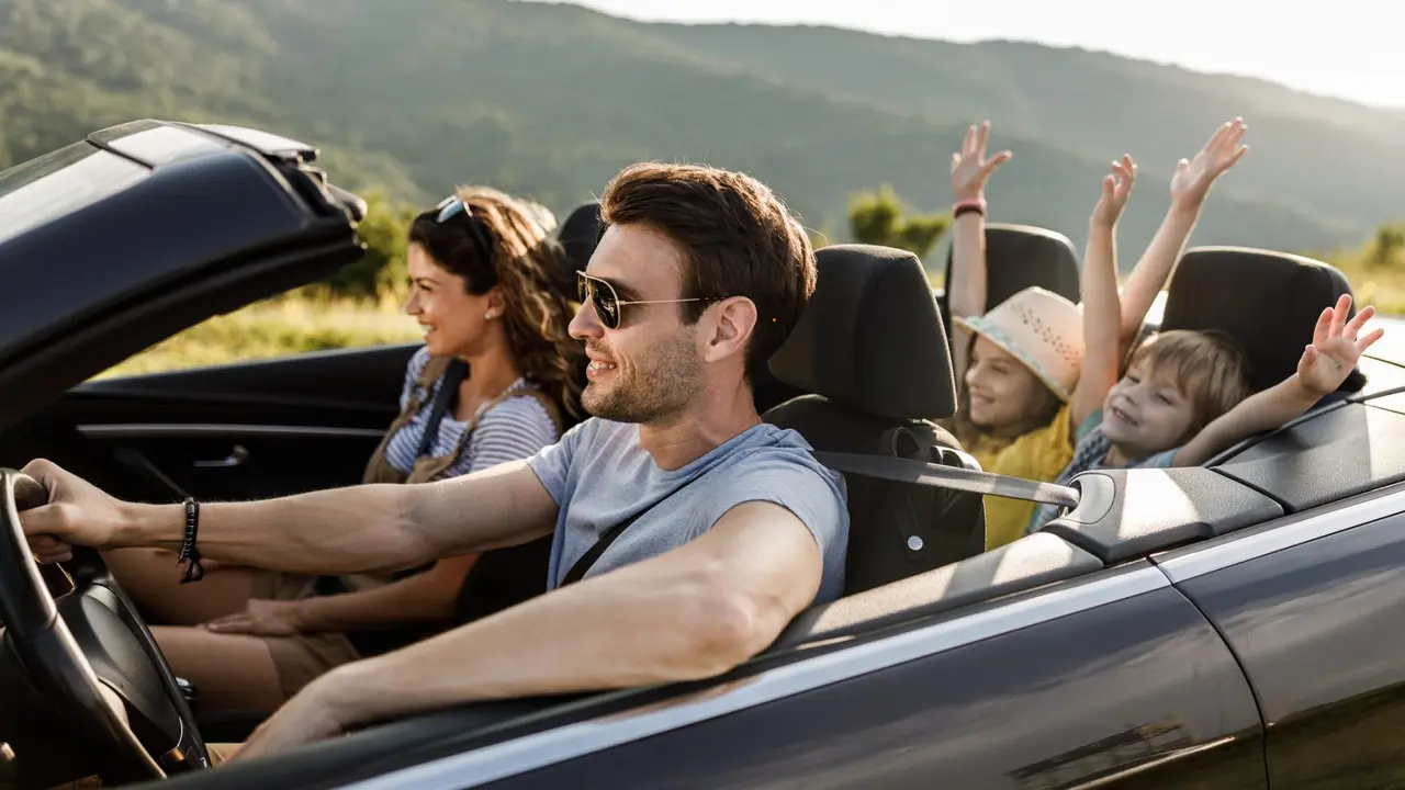 Happy parents and their small kids going on road trip in convertible car.