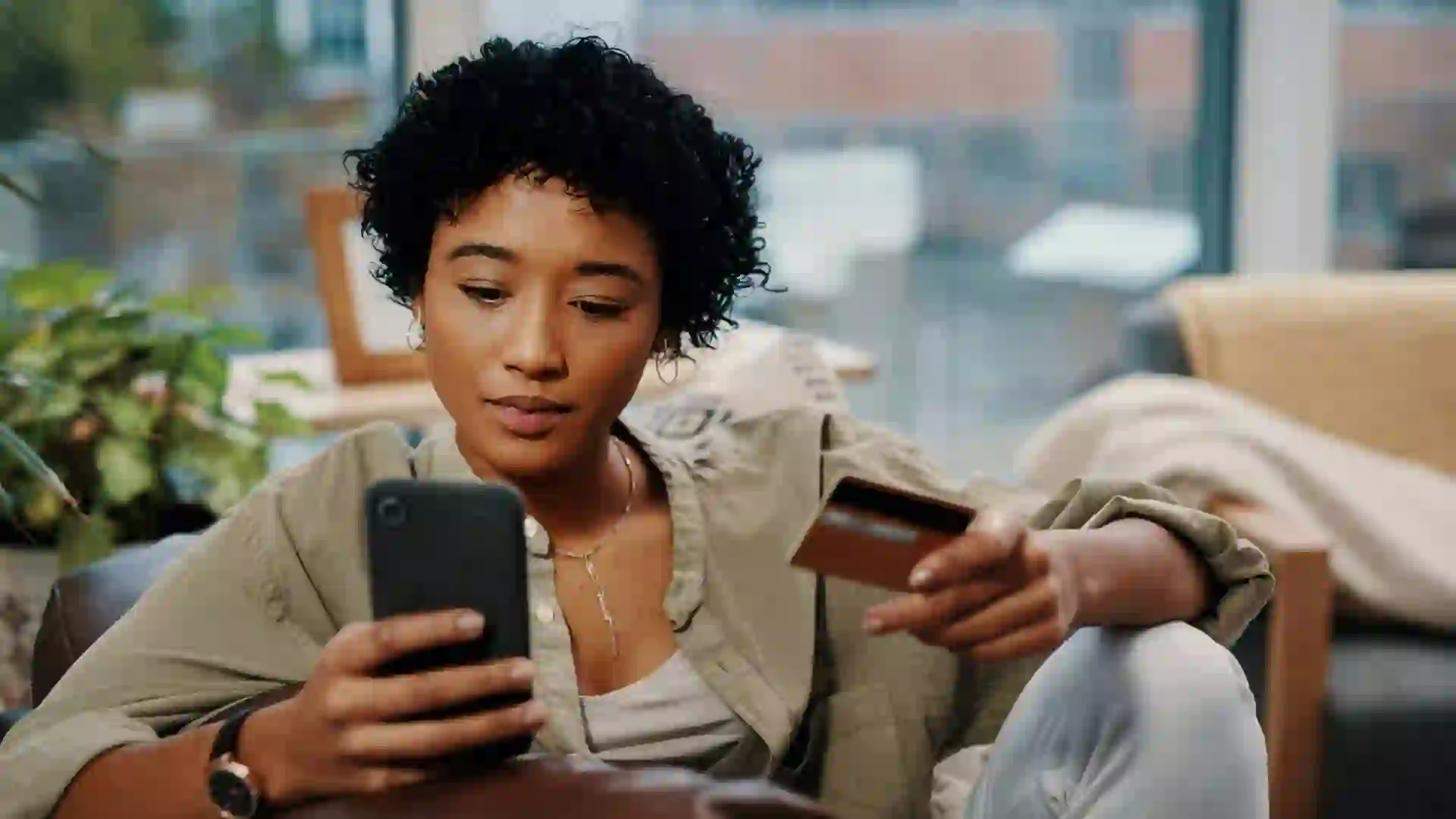 Shot of a young woman holding her credit card while using her cellphone at home.