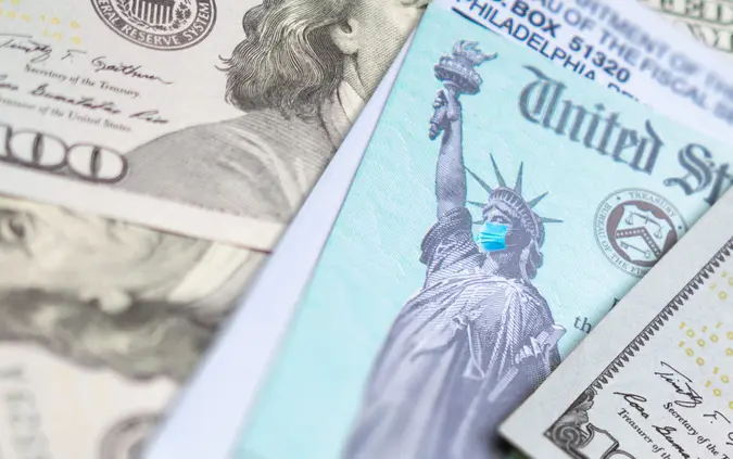 United States IRS Stimulus Check with Statue of Liberty Wearing Medical Face Mask Resting on Money.