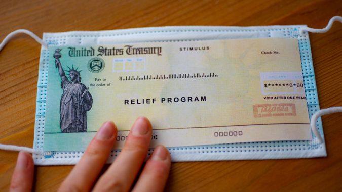 Stimulus relief program check over medical mask on wooden surface.