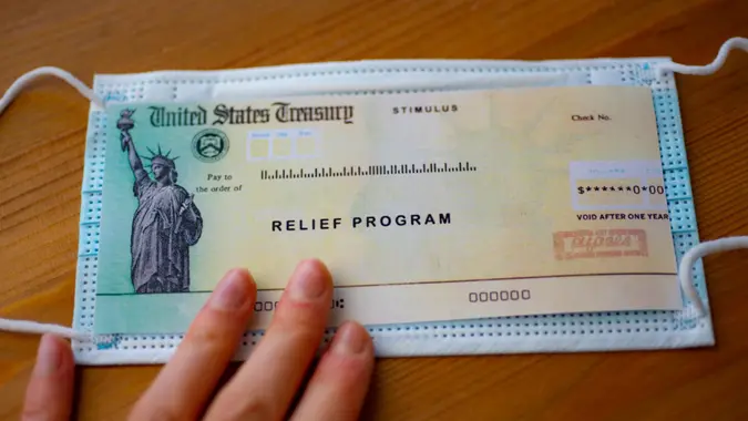 Stimulus relief program check over medical mask on wooden surface.