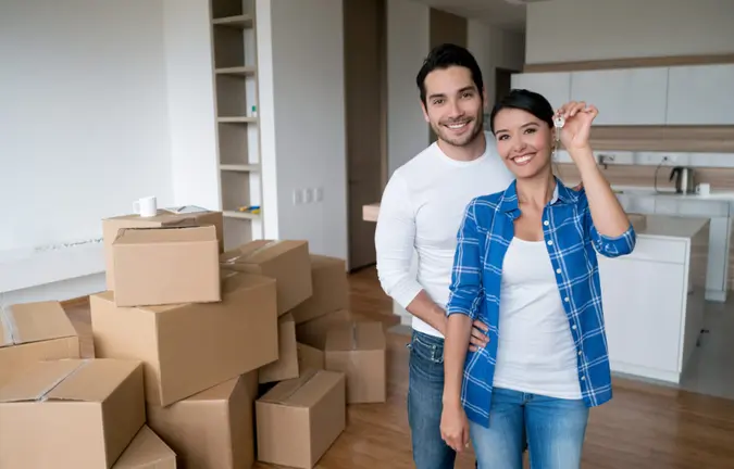 Happy young couple holding keys to their new house while moving and looking at the camera smiling.