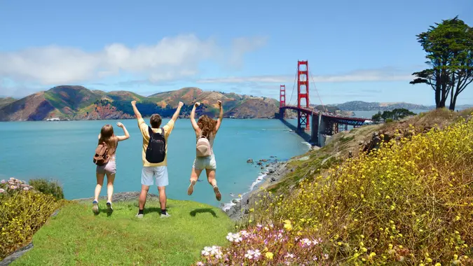 People with hands up jumping and having fun on the top of the mountain, enjoying Golden Gate Bridge view.