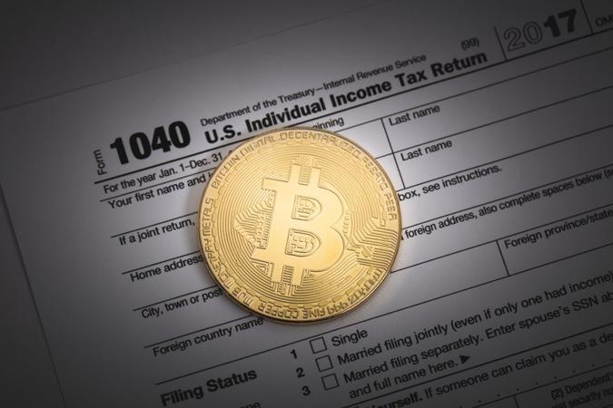 An editorial stock photo of a studio shot of a Bitcoin with some IRS 1040 tax forms.