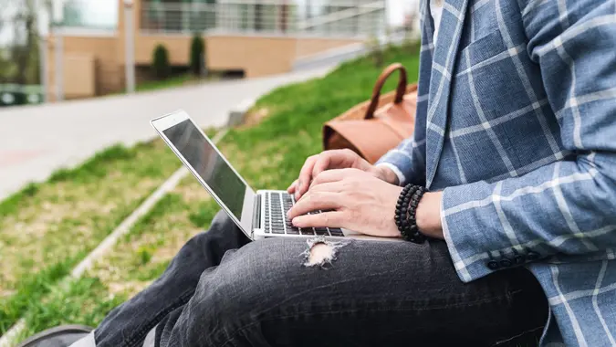 Fashion man sitting on the lawn and working with a laptop. Freelancer, blogger. The life of a modern person stock photo
