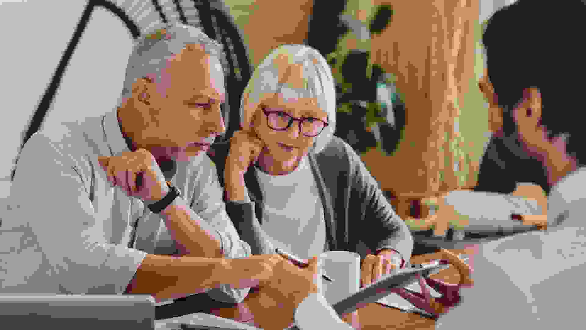 Financial advisor explaining paperwork to elderly retired couple front of desk.