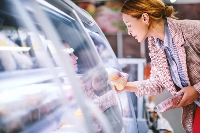 Attractive smiling brunette taking meat from a fridge at local supermarket.