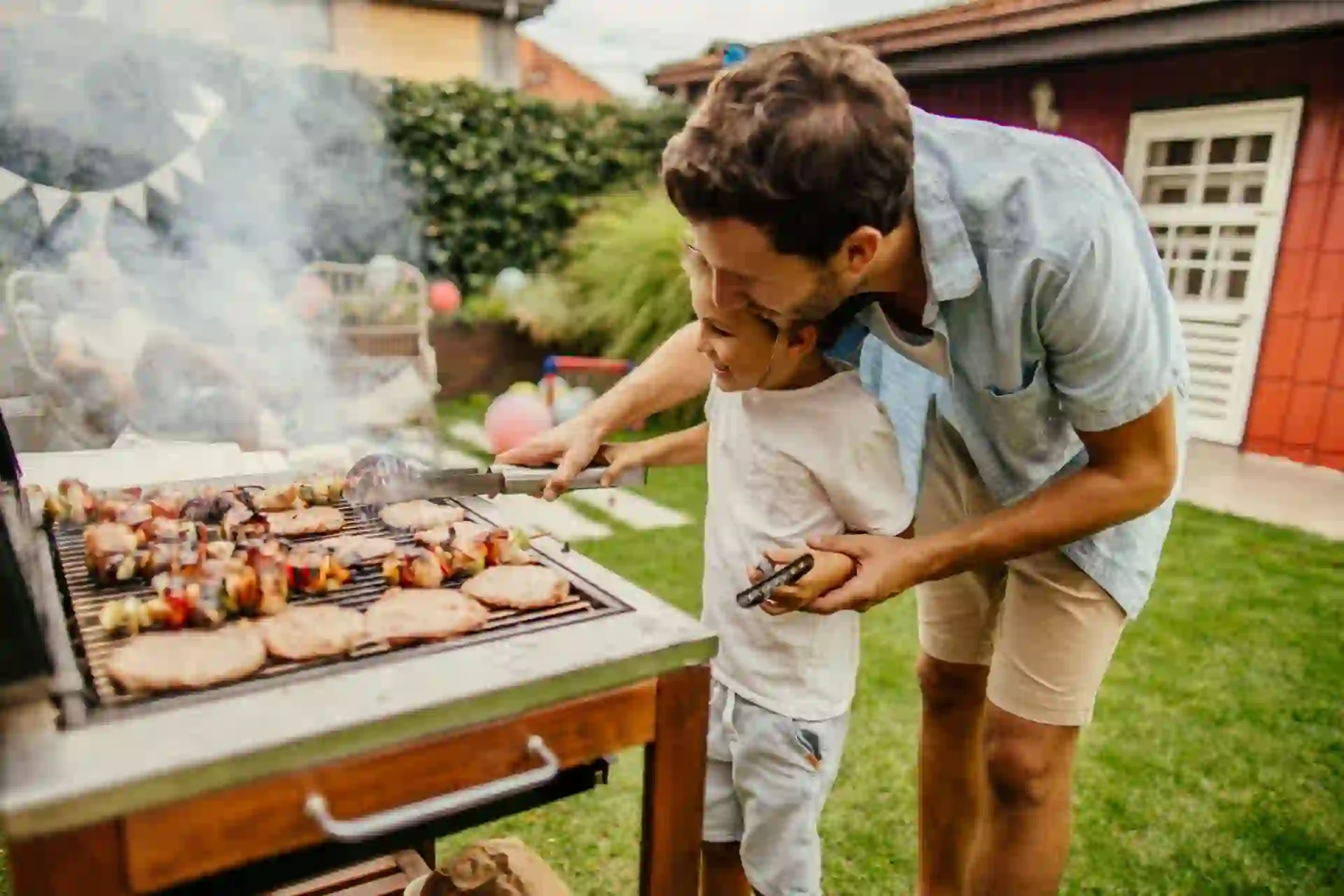 Photo of father and son grilling meat during the barbecue party in their yard.