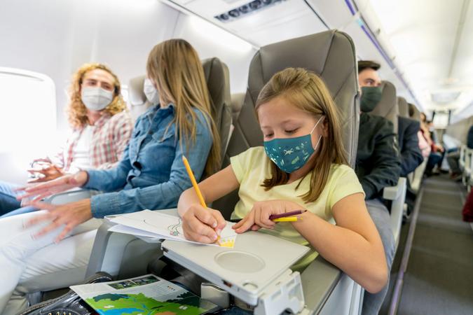 Portrait of a happy girl traveling and coloring in the plane while wearing a facemask â travel concepts.