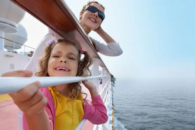 Smiling mother and daughter traveling on big cruise ship, other ship in sea.