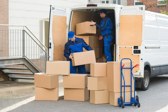 Young delivery men unloading cardboard boxes from truck on street.