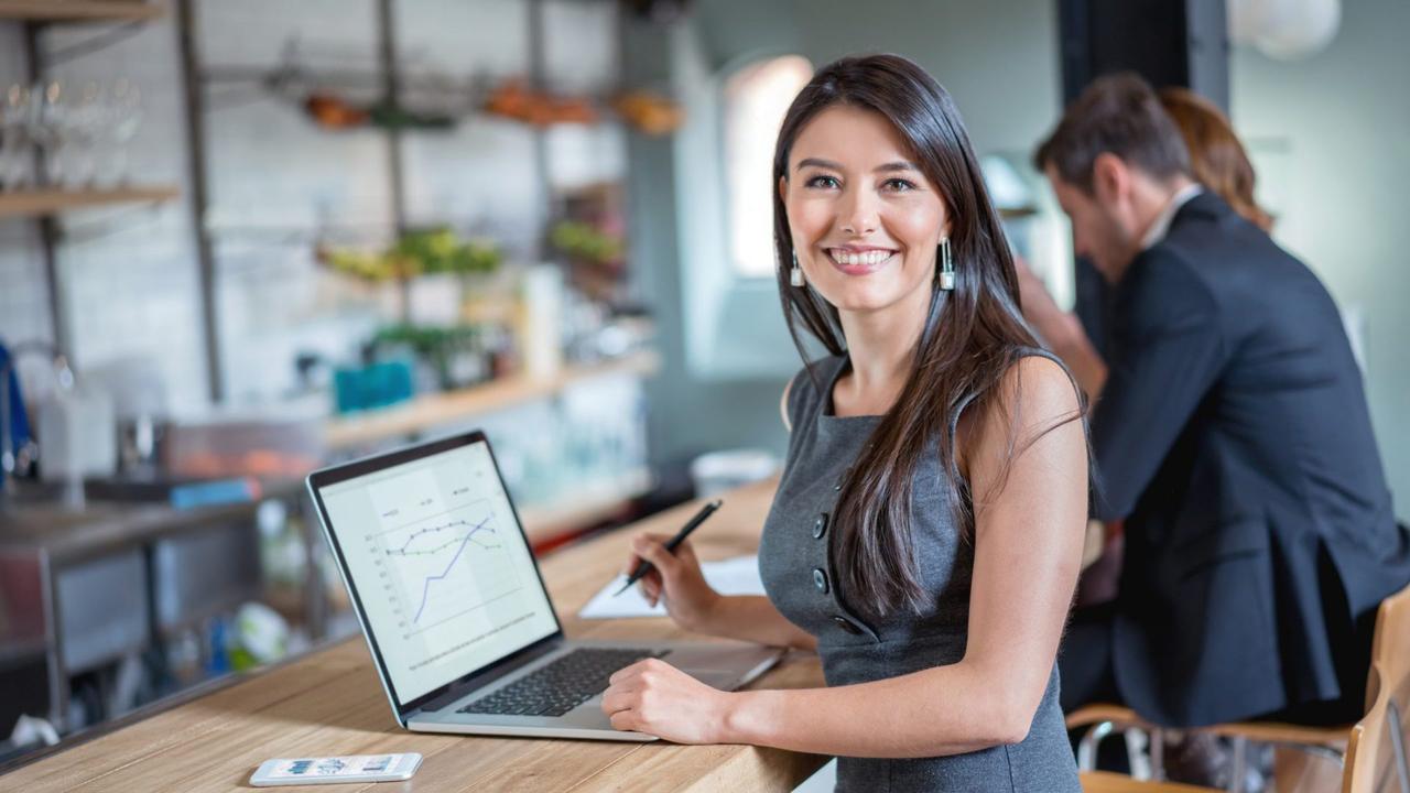 Happy business woman working at a cafe on a laptop and looking at the camera smiling.