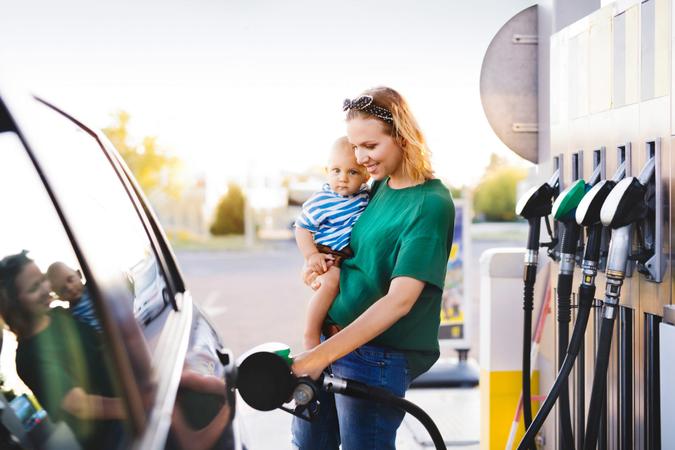 Young mother with baby boy at the petrol station refuelling the car.