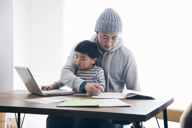 Japanese man in casual clothes writing a document and his son using a laptop on the desk.