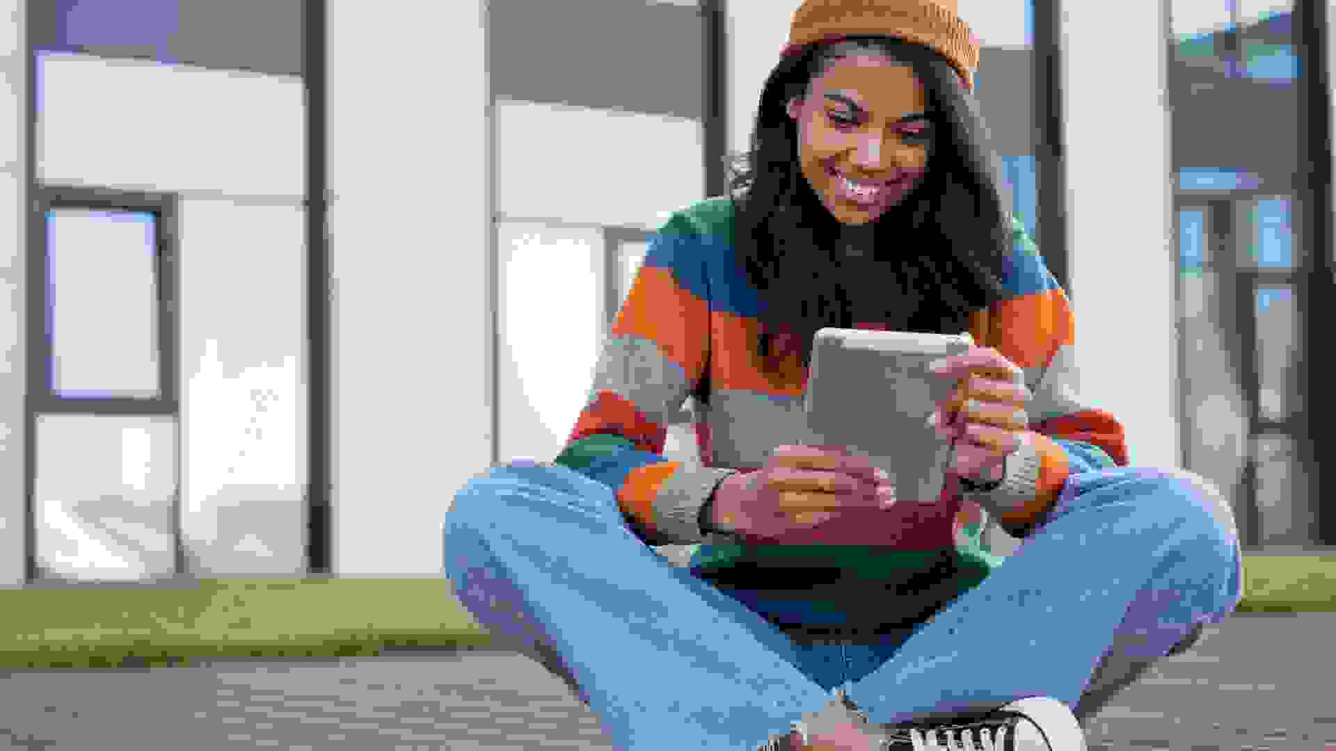 Student studying, learning language, online education concept. Beautiful African American woman using digital tablet, watching movie outdoors stock photo