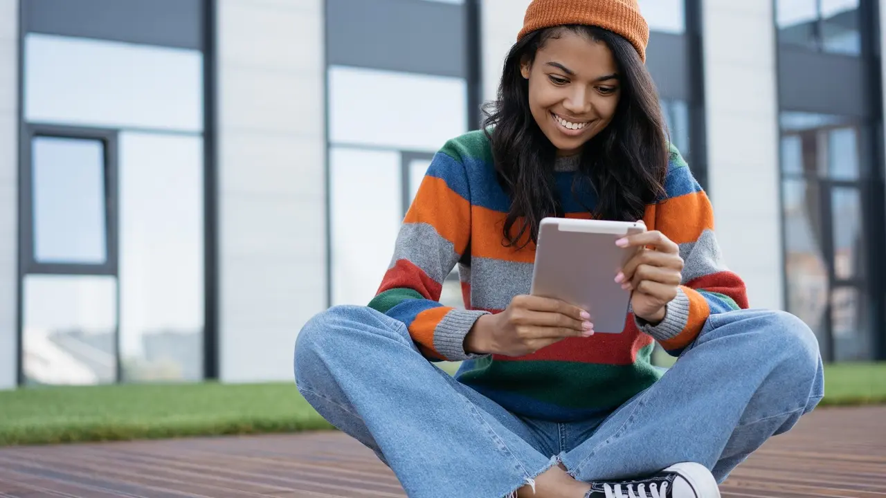 Student studying, learning language, online education concept. Beautiful African American woman using digital tablet, watching movie outdoors stock photo