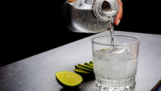 Water being poured into a glass next to sliced lime.