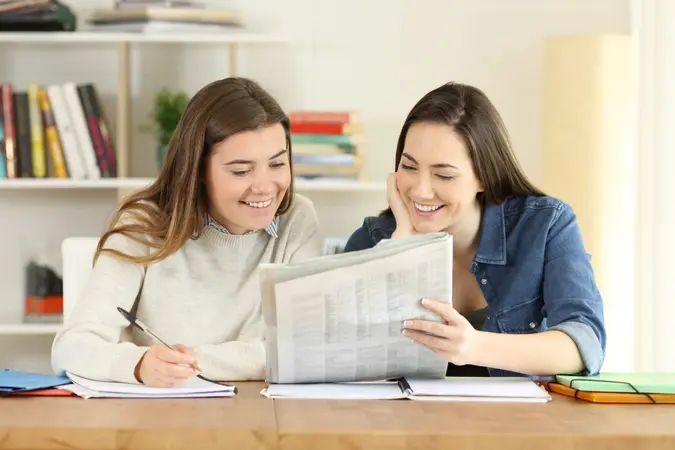 Two happy students talking about newspaper news at home.