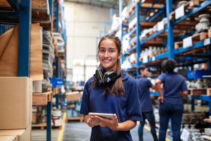 Portrait of a female factory employee with a digital tablet looking at camera and smiling.