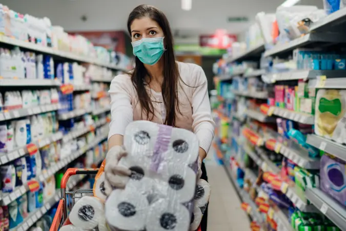 Woman shopper with mask and gloves panic buying and hoarding toilette paper in supply store.