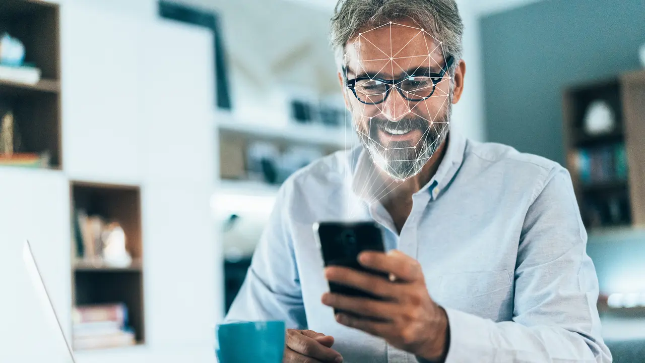 Facial recognition software scans the face of elegant senior man holding smart phone at home.