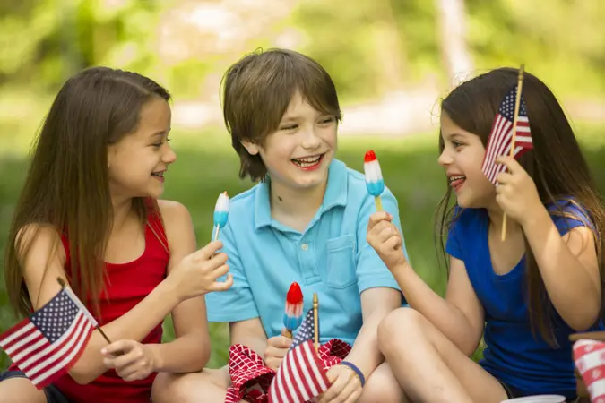 Three American children enjoy a summer picnic outdoors to celebrate USA's Memorial Day, Independence Day, or Labor Day holiday.