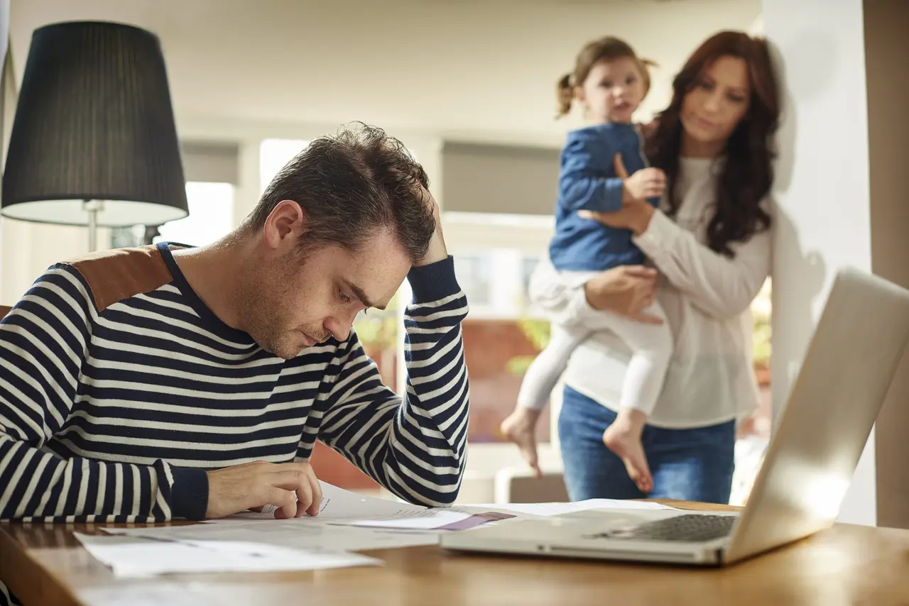 A young husband and father sits at a dining table looking through the household bills and holds his head in despair .