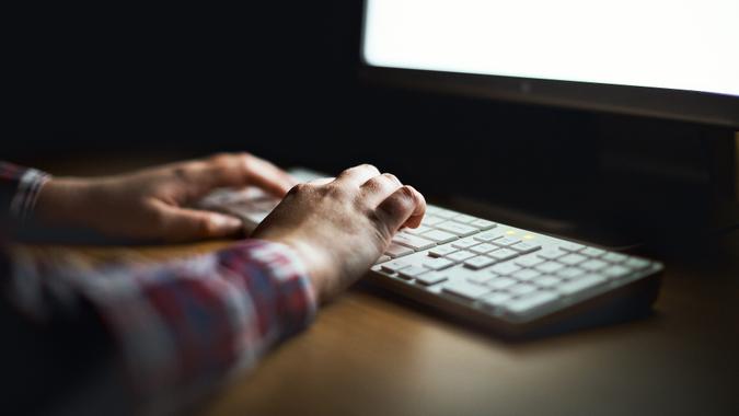 Hands type on computer keyboard lit by monitor stock photo