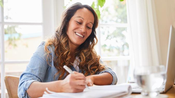 Smiling mature woman writing in a notebook while working from home stock photo
