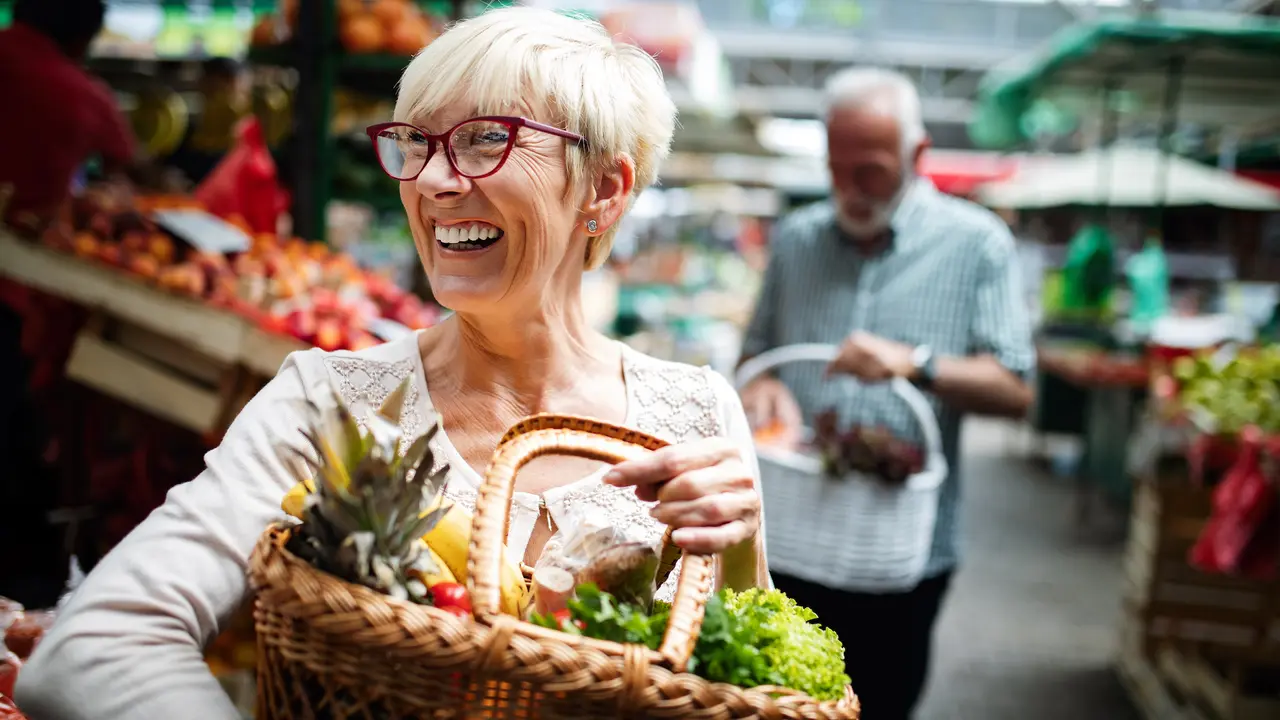 Senior couple smiling and buying fresh vegetables at the local market.