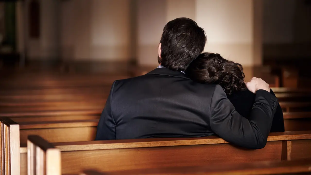 Rearview of a man comforting a woman at a funeral .
