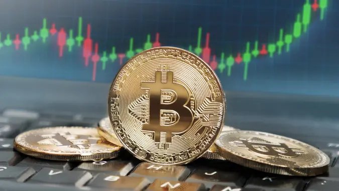 Bitcoins on keyboard with screen in the background displaying rising trend of its value.