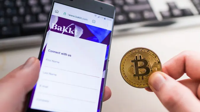 SLOVENIA - JANUARY 7, 2019: Man holding Bitcoin coin and in other hand smartphone with opened Bakkt website.