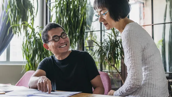 Couple a home looking at home finance documents, man looking up and smiling, woman with serious expression.