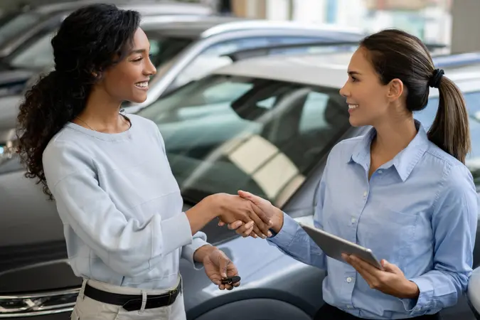 Happy woman buying a car and closing the deal with a handshake with the saleswoman at the dealership.