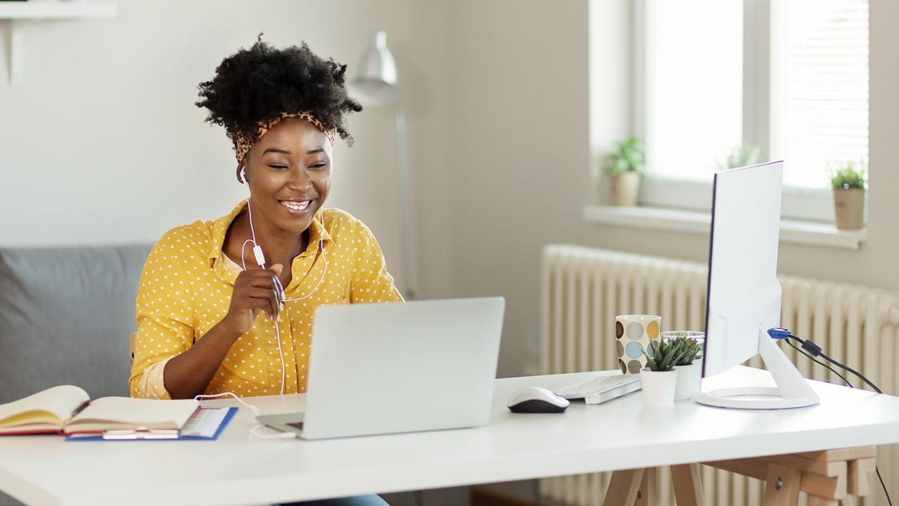 Happy African American Businesswoman Wearing Headphones, Looking at Laptop Screen, Holding Pleasant Conversation With Partners Clients Online, Working Remotely at Workplace.