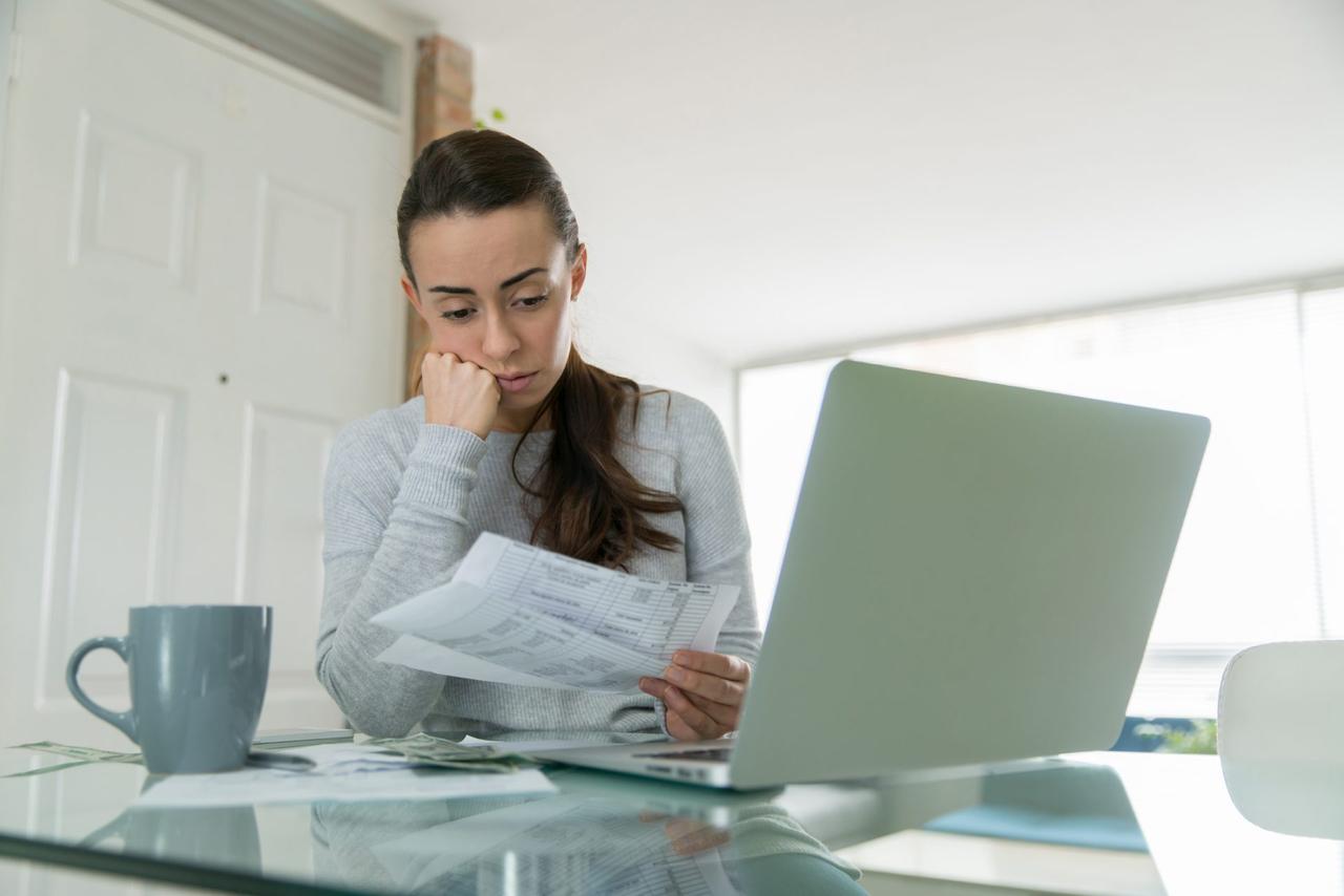 Woman paying her utility bills online and looking worried while staying at home during the pandemic - home finances concepts.