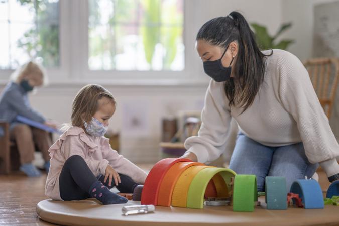 Young girl playing on a play mat at daycare while wearing a mask due to COVID-19.