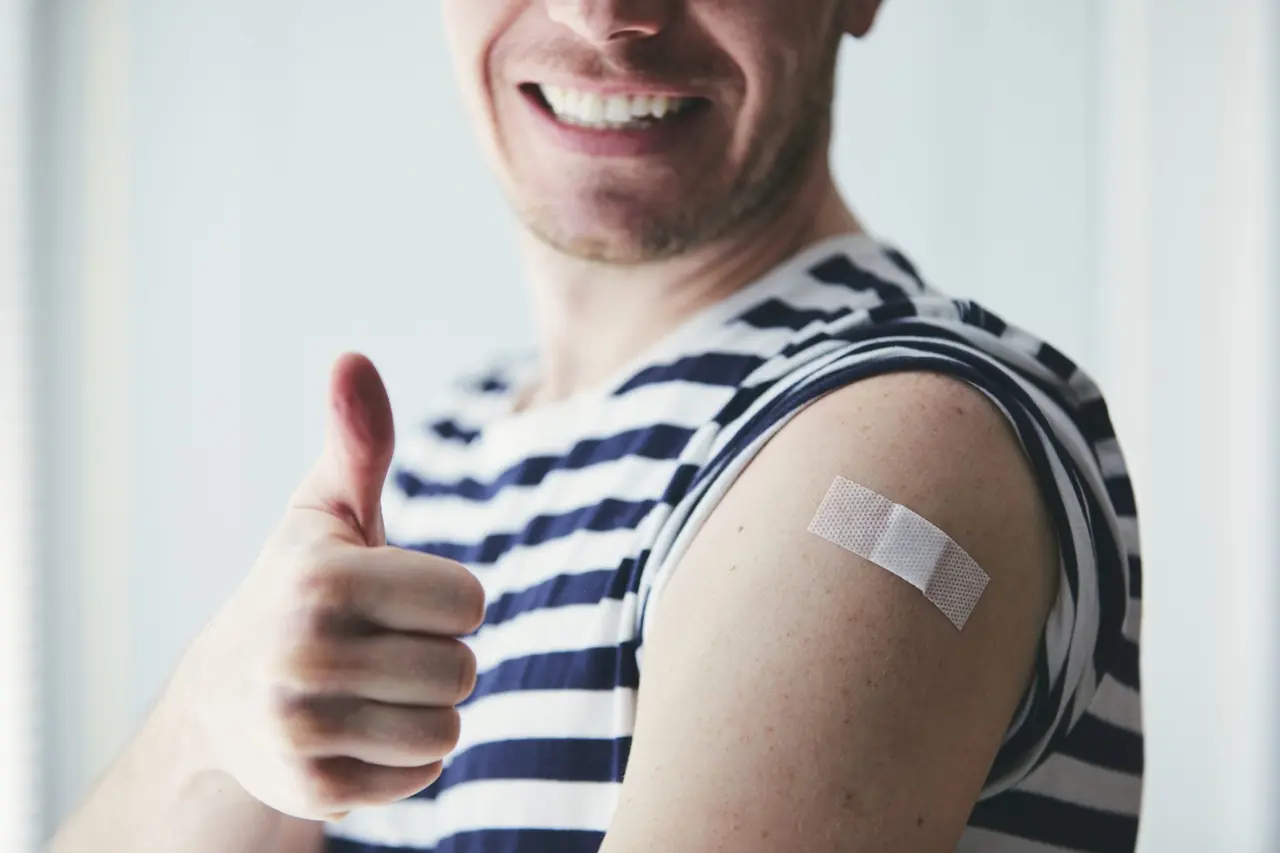 Happy young man showing thumb up and his arm after vaccination.