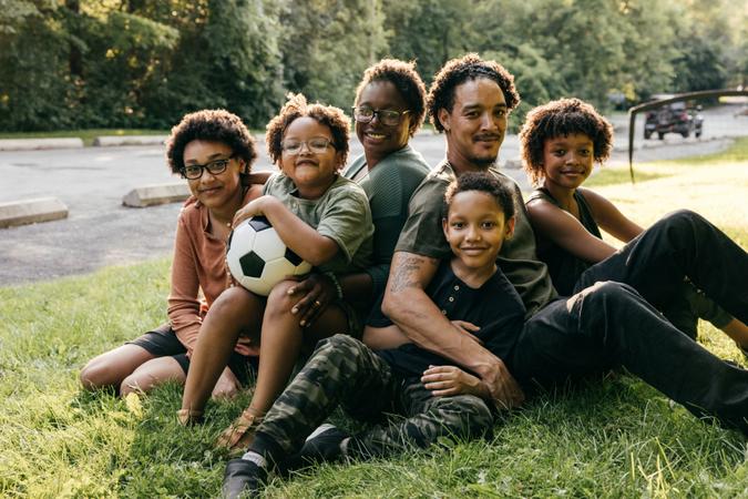 Portrait of black family smiling and looking at the camera, embracing outside in a field.