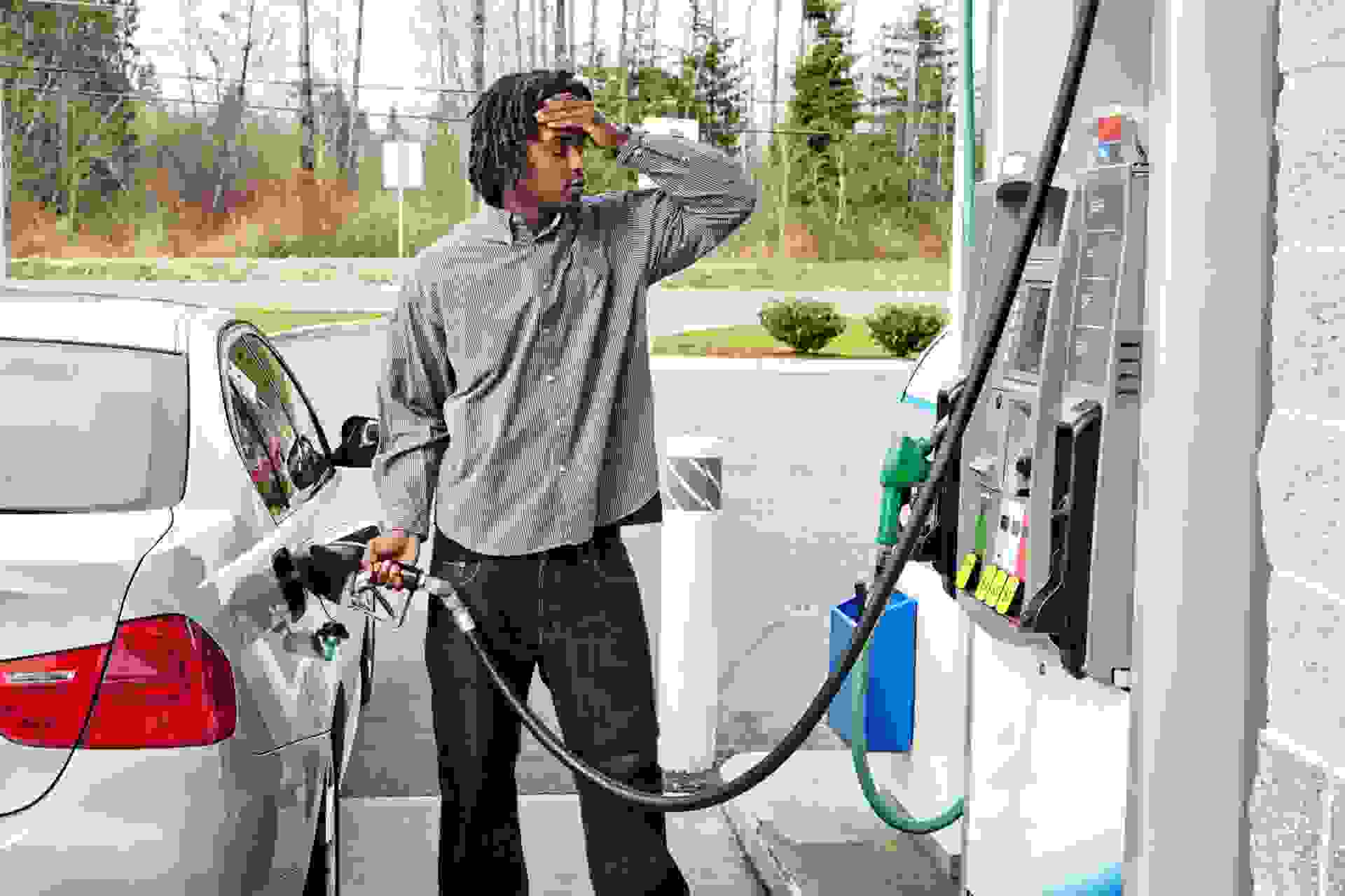 "Photo of a young man watching filling his gas tank, watching in disbelief as the dollar amount climbs on the gas pump display too quickly to comprehend.