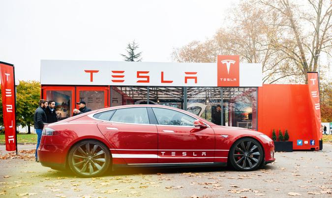 Paris: View from the street of new Tesla Model S showroom parked in front of the showroom with customers admiring the red electric luxury car.