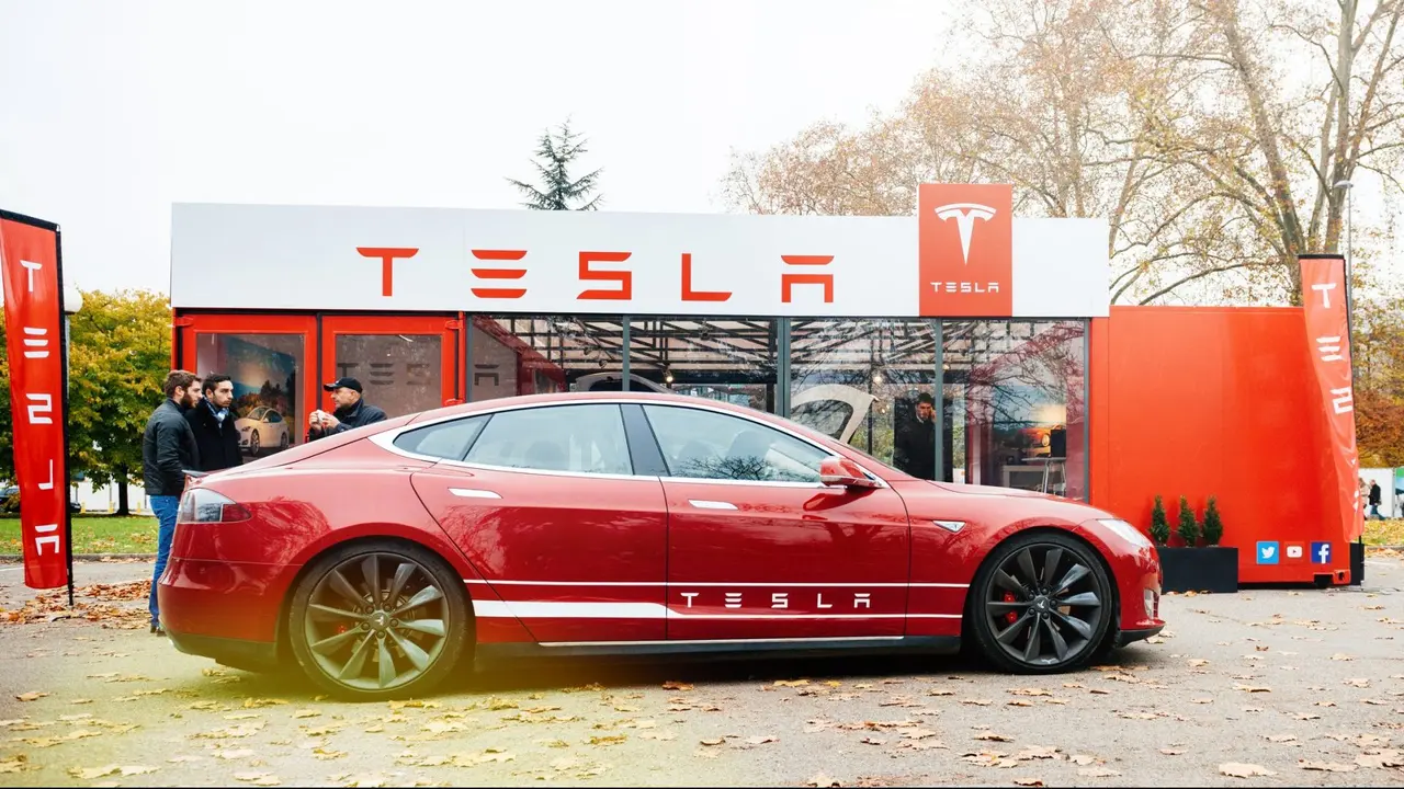 Paris: View from the street of new Tesla Model S showroom parked in front of the showroom with customers admiring the red electric luxury car.
