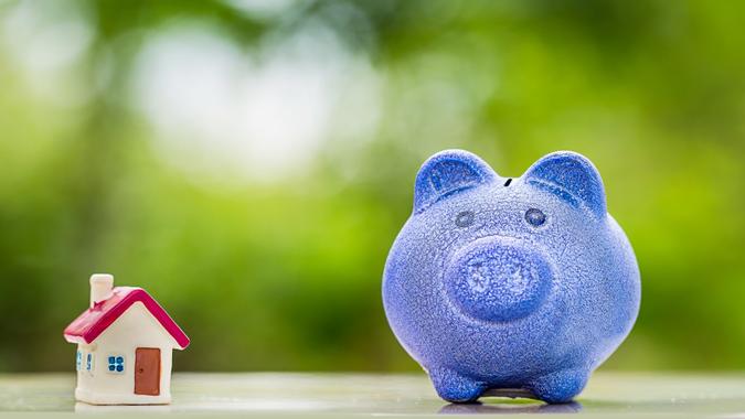 Blue piggy bank with tiny home on wooden table over blurred garden bokeh background. stock photo