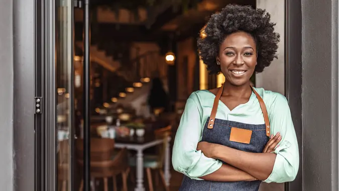 Cheerful female cafe owner standing at the door with her arms crossed.