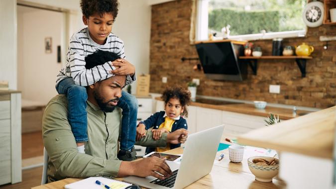 Black stay at home father working on laptop while his kids are demanding his attention. stock photo