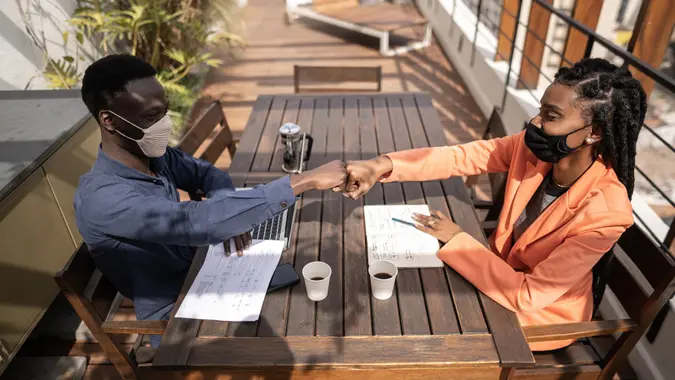 Businessman and businesswoman greeting winth a fist bump - wearing protective face mask stock photo